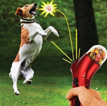 Pet treat launcher in red being used to launch treats towards a jumping dog in a green outdoor setting
