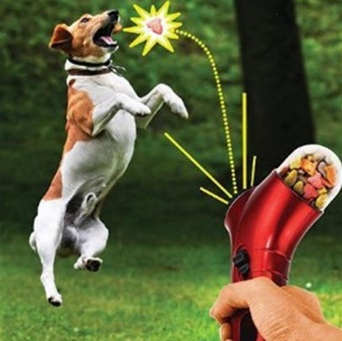 Pet treat launcher in red being used to launch treats towards a jumping dog in a green outdoor setting