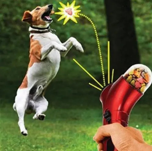 Pet treat launcher in red being used to launch treats towards a jumping dog in a green outdoor setting